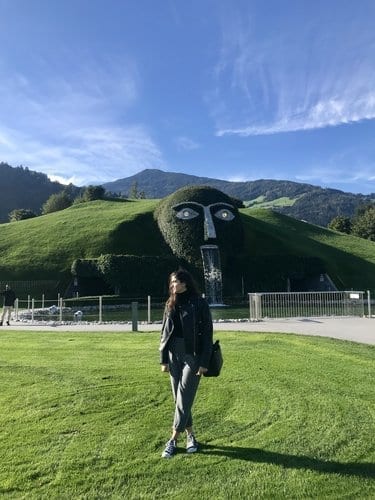 Sara steht in einer grünen Wiese, hinter ihr ein kleiner Wasserfall in den Kristallwelten