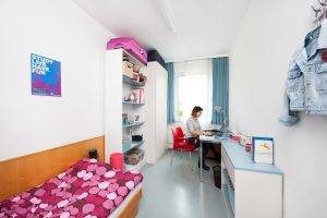 Bewohnerin sitzt lächelnd vor ihrem Laptop im Einzelzimmer