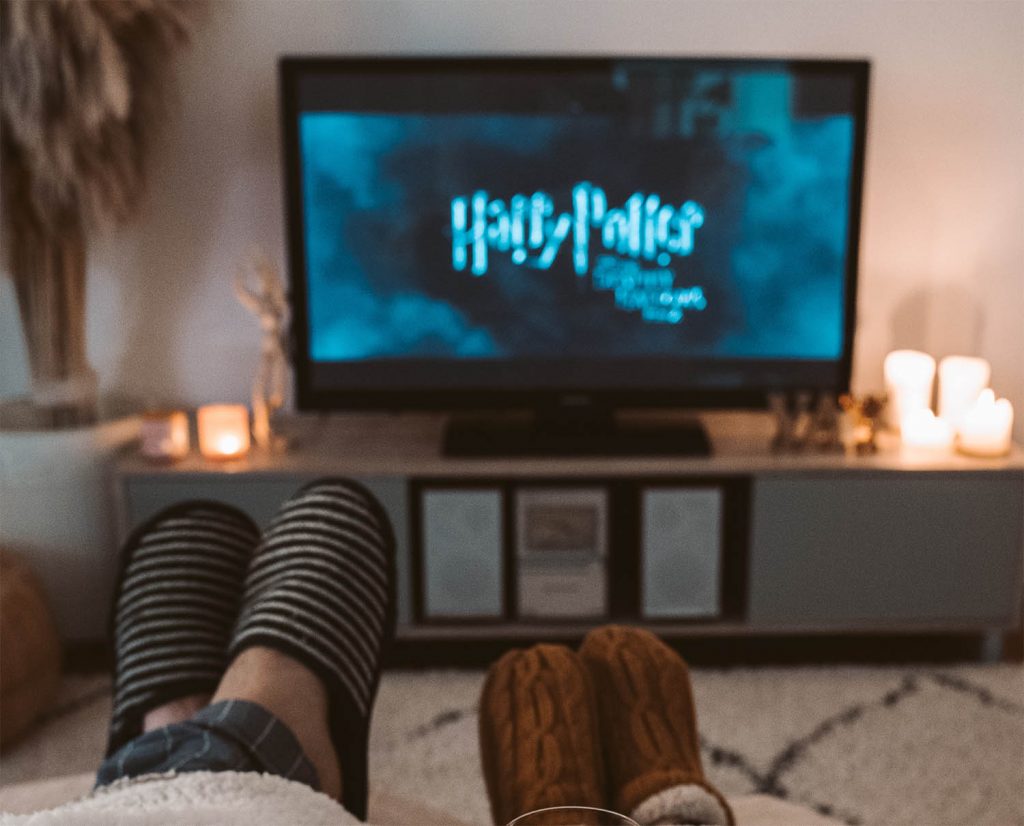 Wohnzimmer, zwei Füße in Hausschuhen, dahinter ein TV mit Harry Potter