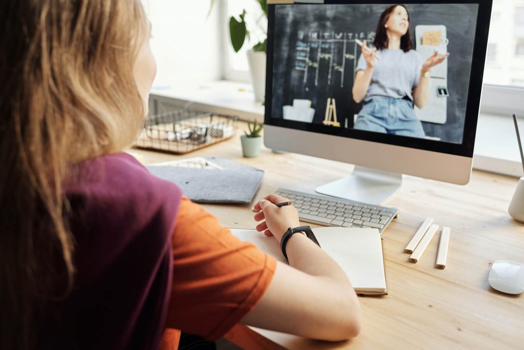 Frau sitz vor einem PC und hat ein Notizbuch am Tisch liegen