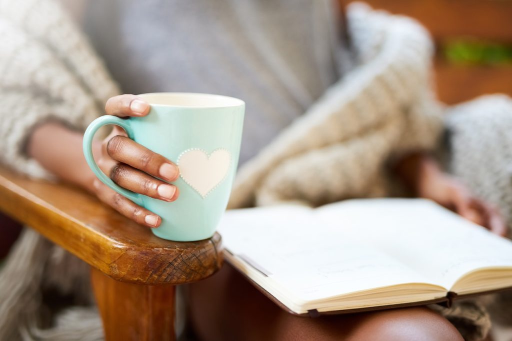 Nahaufnahme von einer Frau mit einem Buch am Schoß, und einer Teetasse in der Hand