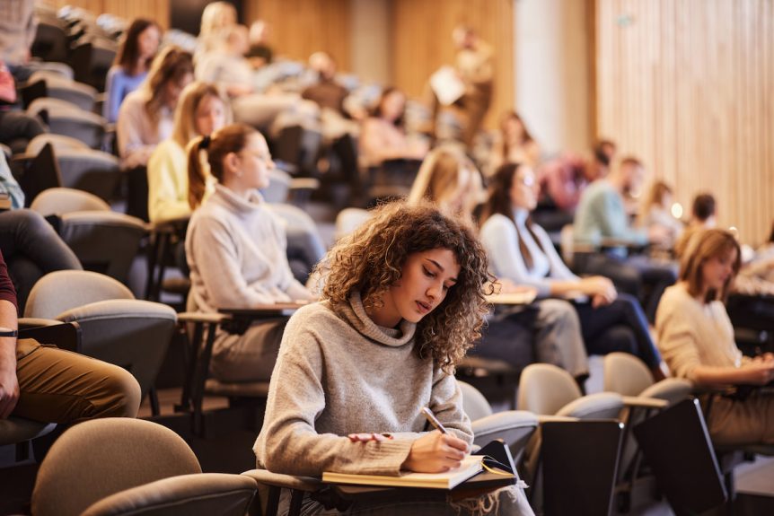 Studentin sitzt im Vorlesungssaal und macht sich Notizen